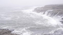 Foggy sea landscape, waves crashing on ocean beach in haze, misty weather. Calm tranquil moody atmosphere, grey monochrome seascape, gloomy dramatic shore cliffs or coast rocks. stormy water surface.