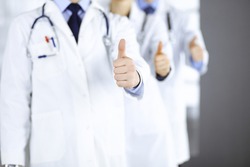 Group of unknown doctors stand as a team with thumbs up in a hospital office. Physicians ready to examine and help patients. Medical help, insurance in health care, best desease treatment and medicine