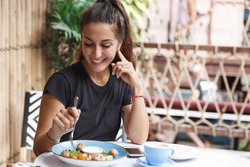 Eating out, lifestyle and travelling concept. Portrait of pretty european woman eating at restaurant table healthy food, drinking coffee, dining alone, smiling, tourist at cafe of her hotel