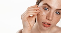 Face of plus size redhead model, woman with freckles, using under eye patches from puffiness, black dark circles, using cosmetic product from wrinkles, white background
