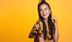 Vacation and tourism. Smiling young woman on holiday, wears bright dress and flower in her hair, looks happy at banner aside, stands over yellow background.