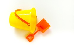 bright yellow child's sand pail on its side with a bright orange shovel isolated on white
