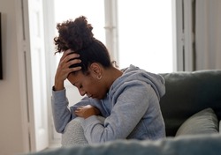 Lonely young African American young woman on sofa feeling pain, exhaustion and sadness. Depressed at home, looking away with sad expressions. In Depression and Mental health concept.