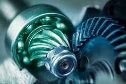 Artistic detail of steel gear wheels inside angle grinder machine in green blue shade. Mechanism of power tool engine with locking nut and ball bearing on cogwheel with pinion. Metallic cogged parts.