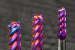 Three steel end mills with beautiful colored nano coating on gray background. Closeup of sharp edges of spiral screw milling cutters with cylindrical shank. Endmill tool teeth detail. Selective focus.