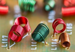 Electronic air-core inductors on beige printed circuit board detail. Closeup of colored spiral copper wire windings of coils inside TV tuner part for receiving radio-frequency signal. Selective focus.