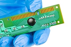Closeup of electronic chip on board in engineer gloved hand isolated on white background. Integrated circuit covered by black epoxy blob and embedded to green PCB with printed wire lines to connector.