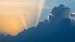 Dramatic sunset with long sunbeams on summer cloudscape at scenic evening dusk. Beautiful contrast between yellow sun beams on clear sky background and dark blue clouds silhouette with white contours.