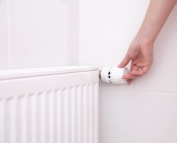 A woman's hand holds the heating thermostat handle. Heating service cost concept, utility price increase