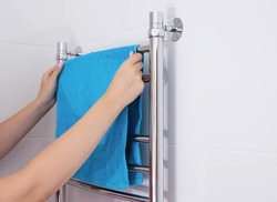 The girl hangs a towel in the bathroom on the heated towel rail. Copy space for text