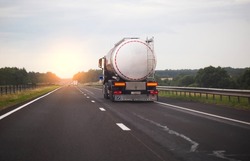 A truck with a semi-trailer transports a dangerous chemical cargo in a tank car on a highway against the background of a sunset. Sanctions in cargo transportation, capacity