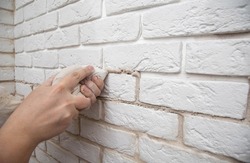filling the seams in a decorative white stone in the form of a brick on the wall. Laying decorative stone on the wall