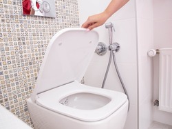A woman's hand holds the toilet lid in the toilet. The concept of cleanliness and hygiene in the bathroom, pleasant smell of freshness