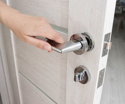 A man's hand opens an interior door with a broken doorknob. Poor quality door hardware, breakage, damage. Close-up