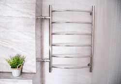 Modern chrome heated towel rail with warm water on a tiled wall. There is a flower on the shelf. Beautiful bathroom item. Close-up