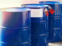 the close-up shot of blue color hazardous dangerous chemical drum barrels ,have warning labels of corrosive & flammable liquid in daylight on daytime.