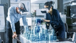Male and Female Architects Wearing  Augmented Reality Headsets Work with 3D City Model. High Tech Office Professional People Use Virtual Reality Modeling Software Application.