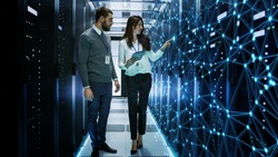 Female and Male IT Engineers Discussing Technical Details in a Working Data Center/ Server Room with Internet Connection Visualisation.