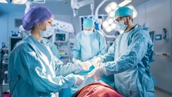 Shot in the Operating Room Assistant Hands out Instruments to Surgeons During Operation. Surgery in Progress. Professional Medical Doctors Performing Surgery.