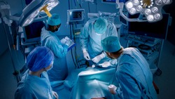High Angle Shot of Diverse Team of Professional surgeon,  Assistants and Nurses Performing Invasive Surgery on a Patient in the Hospital Operating Room. Real Modern Hospital with Authentic Equipment.