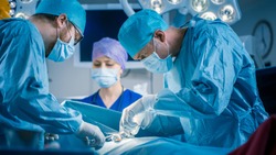 In the Hospital Operating Room Diverse Team of Professional Surgeons and Nurses Suture Wound after Successful Surgery.