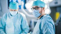 Portrait Shot of a Surgeon Looking into Camera. Diverse Team of Professional surgeons, Assistants and Nurses Performing Invasive Surgery on a Patient in the Hospital Operating Room.