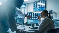 Two Scientists in the Brain Research Laboratory work on a Project, Using Personal Computer with MRI Scans Show Brain Anomalies. Neuroscientists at Work.