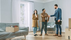 Professional Real Estate Agent Shows Bright New Apartment to Young Couple. Successful Young Couple Becoming Homeowners, Seal the Deal with Real Estate Broker by Handshake. Bright Home with Big Windows