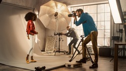 Behind the Scenes on Photo Shoot: Beautiful Black Model Posing for a Photographer, he Takes Photos with Professional Camera. Stylish Fashion Magazine Photoshoot with Pro Equipment in a Studio