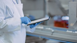 Quality Supervisor or Food Technician is Inspecting the Automated Production at a Food Factory. Close Up Shot of Employee Using Tablet Computer for Work. He Types In Data While Wearing Latex Gloves.