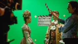 On Big Film Studio Professional Crew Shooting Period Costume Drama Movie. On Set: Camera Assistant Using Clapperboard, Cameraman Shooting Green Screen Scene with Two Actors in Renaissance Clothes