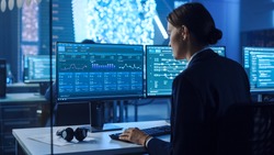 Confident Female Data Scientist Works on Personal Computer in Big Infrastructure Control and Monitoring Room with Neural Network. Woman Engineer in an Office Room with Colleagues.