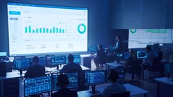 Team of Professional Big Data Business Traders Work on Desktops with Screens Showing Charts, Graphs, Infographics, Technical Neural Data and Statistics. Low Key Control and Monitoring Room.