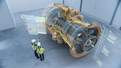 Industry 4.0 Two Engineers Standing and Talking in Factory Workshop with Augmented Reality 3D Model Concept of Giant Turbine Engine. Graphics Visualization. High Angle Shot. VFX Special Visual Effects