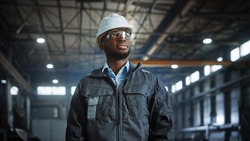 Portrait of Professional Heavy Industry Engineer Worker Wearing Uniform, Glasses, Hard Hat in Steel Factory. Smiling African American Industrial Specialist Standing in Metal Construction Manufacture.