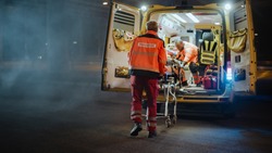 Team of EMS Paramedics React Quick to Provide Medical Help to Injured Patient and Get Him in Ambulance on a Stretcher. Emergency Care Assistants Arrived on the Scene of a Traffic Accident on a Street. Blur