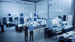 Modern Factory: Two Engineers Use Digital Tablet Computer with Augmented Reality Visualizing Workshop Room Mapping, Floor Layout. Facility with High-Tech CNC Machinery and robot arm. High Angle