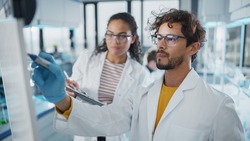 Medical Science Laboratory: Handsome Latin Male Scientist Writes Detailed Project Data Analysis on the Board, His Black Female Colleague Talks. Young Scientists Solving Problems.