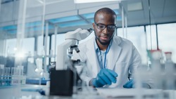 Modern Medical Research Laboratory: Portrait of Male Scientist Using Microscope, Writing Down Analysis Information. Advanced Scientific Lab for Medicine, Biotechnology, Microbiology Development