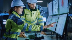 Industry 4.0 Modern Factory: Project Engineer Talks to Female Operator who Controls Facility Production Line, Uses Computer with Screens Showing AI, Machine Learning Enhanced Assembly Process