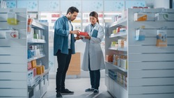Pharmacy Drugstore: Female Asian Pharmacist Helping Latin Male Customer with Recommendation, and Advice to Buy Medicine, Drugs, Vitamins. Modern Pharma Store Shelves with Health Care Products