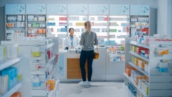 Pharmacy Drugstore: Beautiful Young Woman Buying Medicine, Drugs, Vitamins Stands next to Checkout Counter. Female Cashier in White Coat Serves Customer. Shelves with Health Care Products