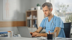 Experienced Male Nurse Wearing Blue Uniform Working on Laptop Computer at Doctor's Office. Medical Health Care Professional Working On Battling Stereotypes to Gender Diversity in Nursing Career.