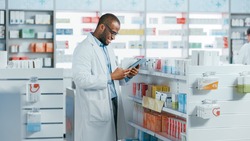 Pharmacy: Portrait of Professional Black Pharmacist Uses Digital Tablet Computer, Checks Inventory of Medicine, Drugs, Vitamins, Health Care Products. Druggist in Drugstore Store.