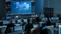 Group of People in Mission Control Center Trying to Establish Video Connection on a Big Screen with an Astronaut on Board of a Space Station. Flight Control Scientists Sit in Front Computer Displays.