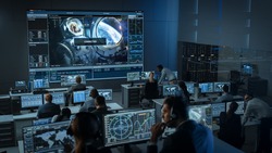 Group of People in Mission Control Center Establish Successful Video Connection on a Big Screen with an Astronaut on Board of a Space Station. Flight Control Scientists Sit in Front Computer Displays.
