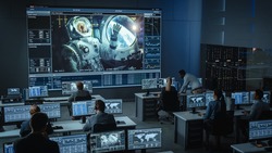 Group of People in Mission Control Center Establish Successful Video Connection on a Big Screen with an Astronaut on Board of a Space Station. Flight Control Scientists Sit in Front of Computers.