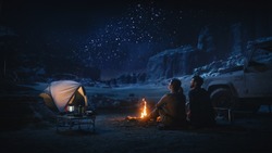 Happy Couple Tent Camping in the Canyon, Sitting by Campfire Watching Night Sky with Milky Way Full of Bright Stars. Two Travelers In Love On a Romantic Vacation Trip. Back View Shot