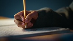 Authentic Close Up Shot of a Young Person Writing with Pencil in Notebook. Teenager Making Homework for School. Education Concept.