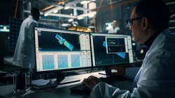 Male Engineer Uses Computer while Working on Satellite Construction. Aerospace Agency: Scientist is Using Computer Software for Programming and Assembly of Spacecraft for Space Exploration Mission.
